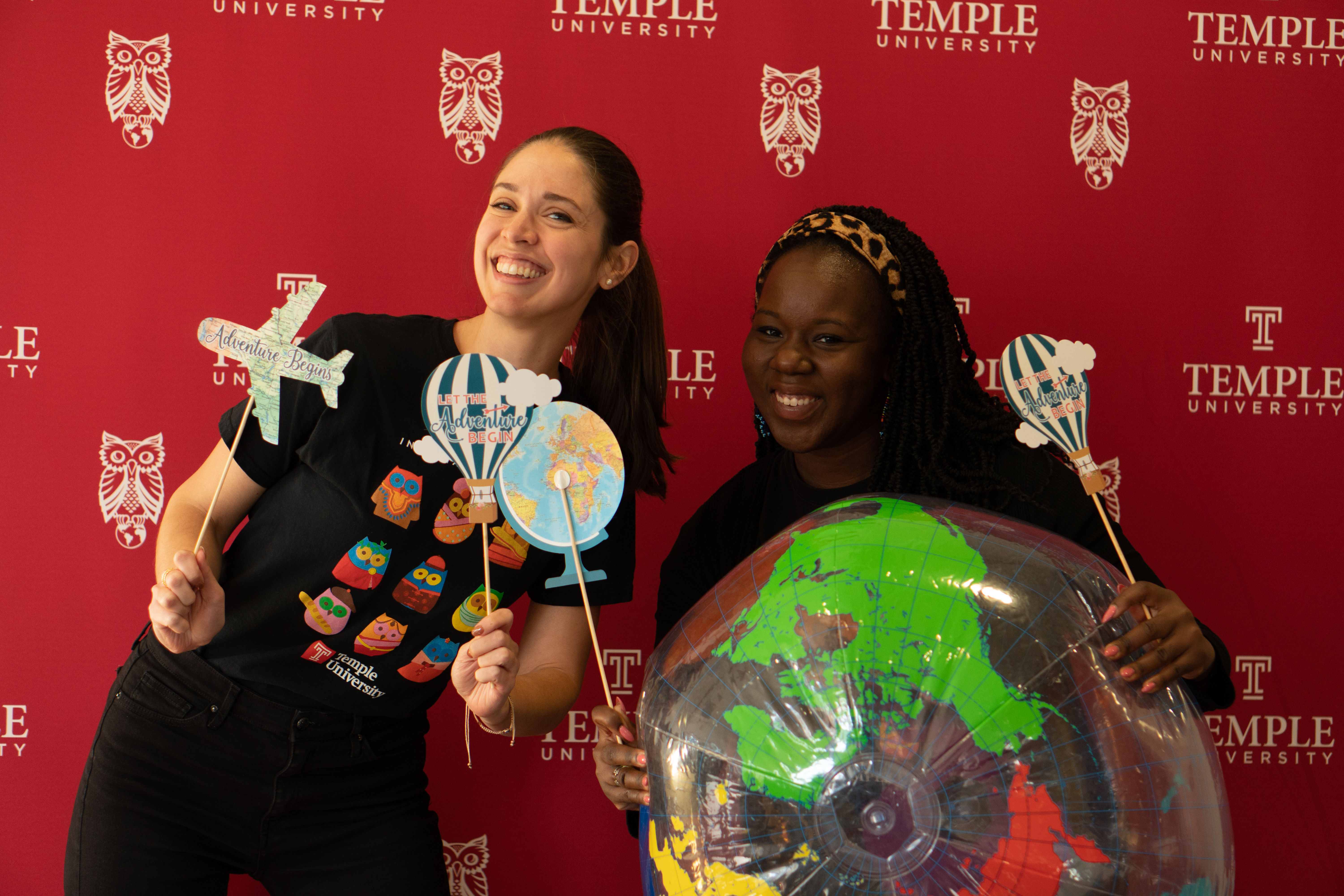 Two student workers holding an inflatable transparent globe ball and smiling into the camera, waving props.
