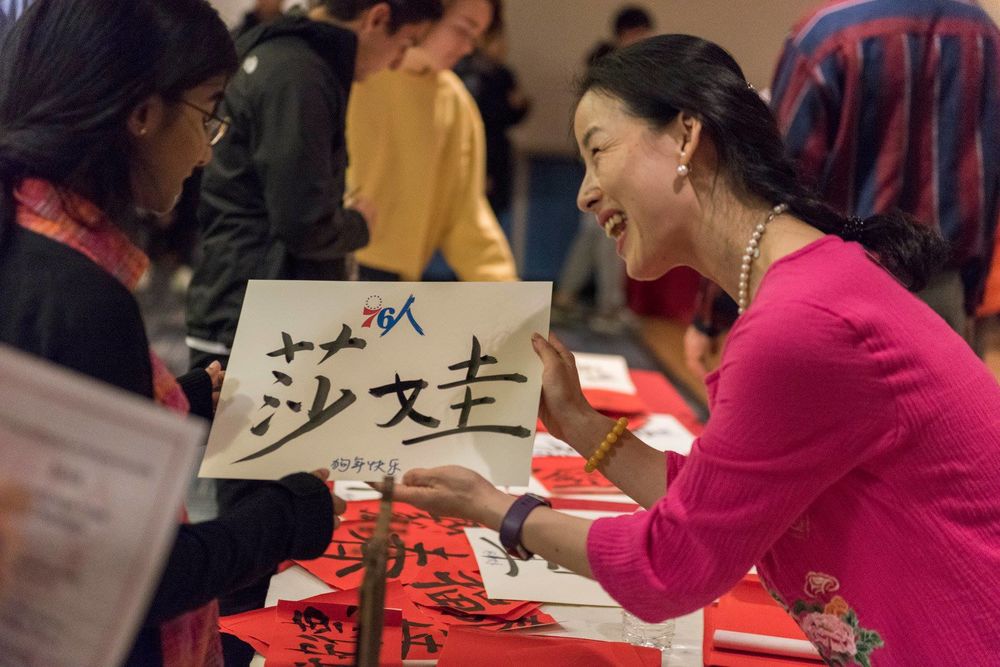 A teacher shows a student Chinese-style calligraphy across a table.